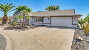 A single-story house with a garage, palm trees, and a well-maintained driveway. - Quiet Sun City West Home - Near Surprise Stadium! (Sun City West)