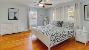 Ein Schlafzimmer mit Bett, Nachttisch, Kommode, Deckenventilator und einem Fenster mit Vorhängen.