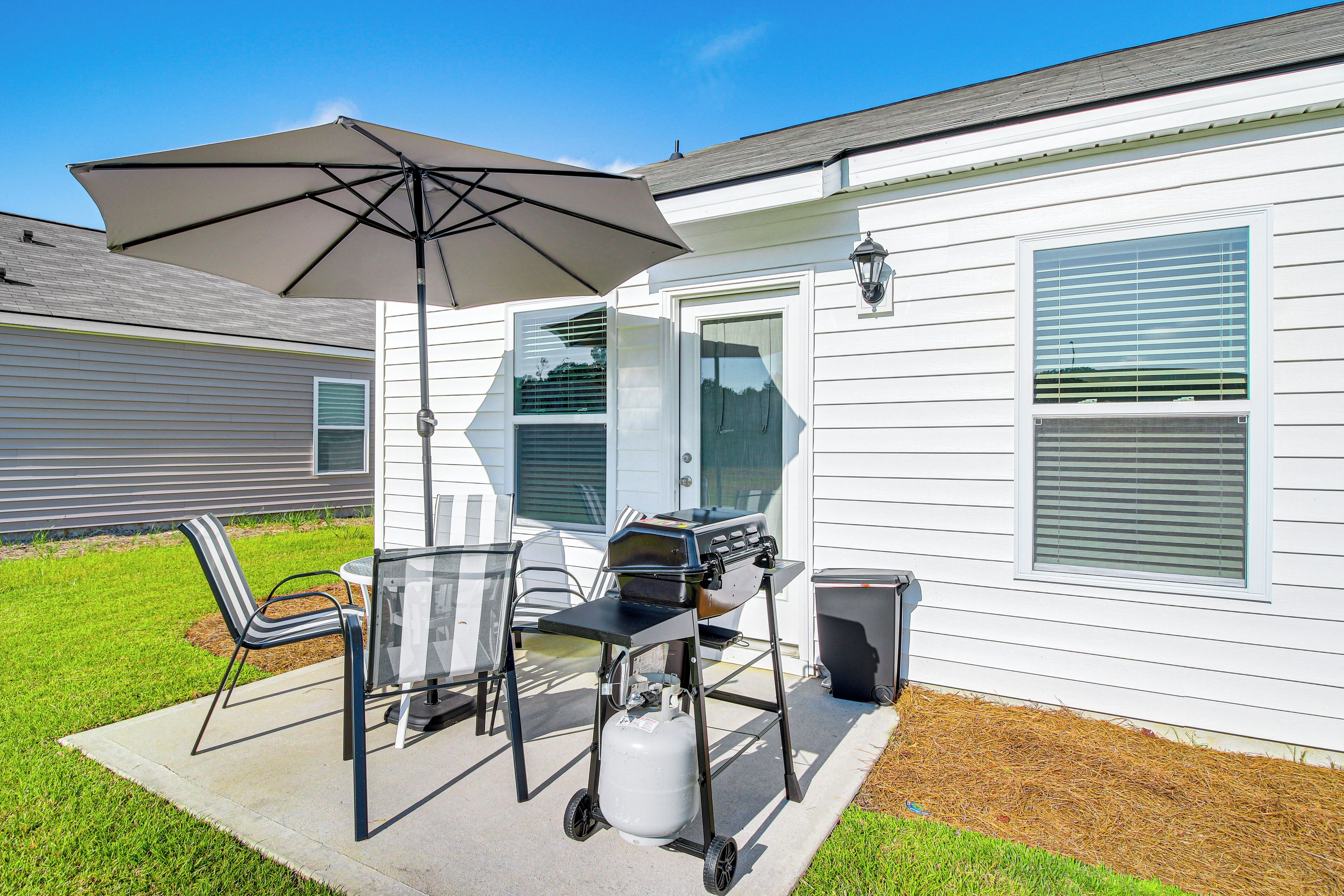 A patio with a grill, chairs, and an umbrella.