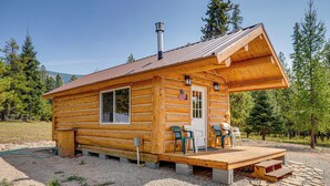 A log cabin with a porch, two chairs, and a small deck. - Mtn Views & Fireplace: Cozy Trout Creek Tiny Home (Trout Creek)