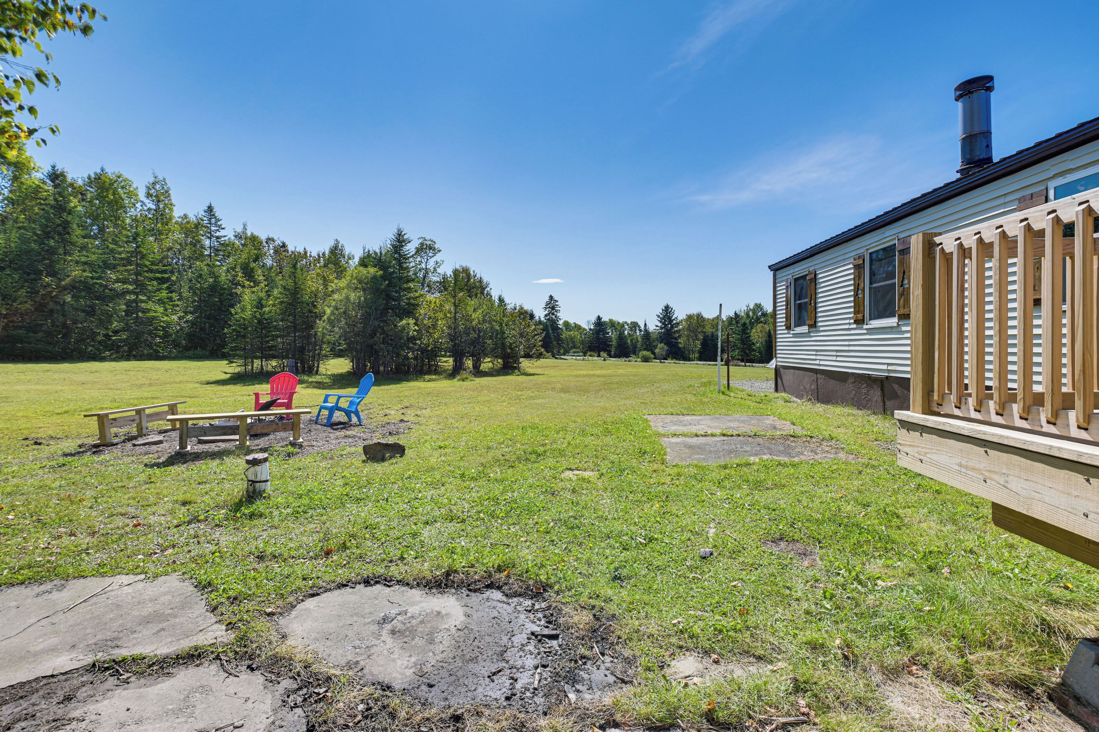A grassy yard with a wooden deck, a picnic table, and a red chair.
