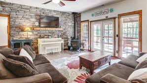 A cozy living room with a stone wall, a fireplace, a ceiling fan, and a large window. - Idaho Family Home ~ 11 Mi to Lake Pend Oreille (Cocolalla)