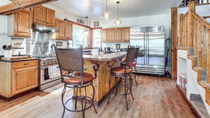 A kitchen with wooden cabinets, a stainless steel refrigerator, and a bar area with stools. - Idaho Family Home ~ 11 Mi to Lake Pend Oreille (Cocolalla)