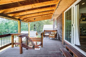 A wooden deck with a bench and a wicker chair, a glass door leading inside, and a view of a house in the background.