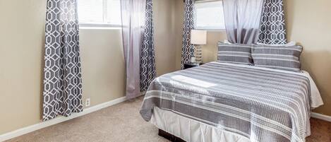 A bedroom with a bed, curtains, a nightstand, and a lamp.