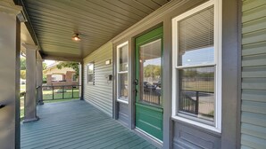 A covered porch with a green door and windows, a metal railing, and a brick building in the background. - Hopkinsville Home: Walk to Downtown! (Hopkinsville)