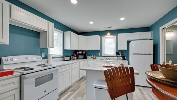 A modern kitchen with white cabinets, a white refrigerator, and a wooden dining table. - Hopkinsville Home Near Parks & Museums! (Hopkinsville)