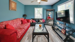 A living room with a red sofa, a glass coffee table, a ceiling fan, a TV, and a window with blinds. - Hopkinsville Home Near Parks & Museums! (Hopkinsville)