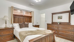 Een slaapkamer met een houten bed, een nachtkastje, een dressoir en een spiegel.