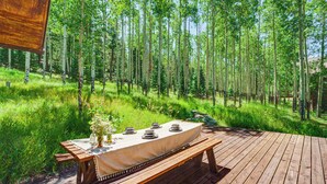 A wooden deck with a table set for dining, surrounded by a forest. - Mountain-view Ranch w/ 200 Acres in Angel Fire (Angel Fire)