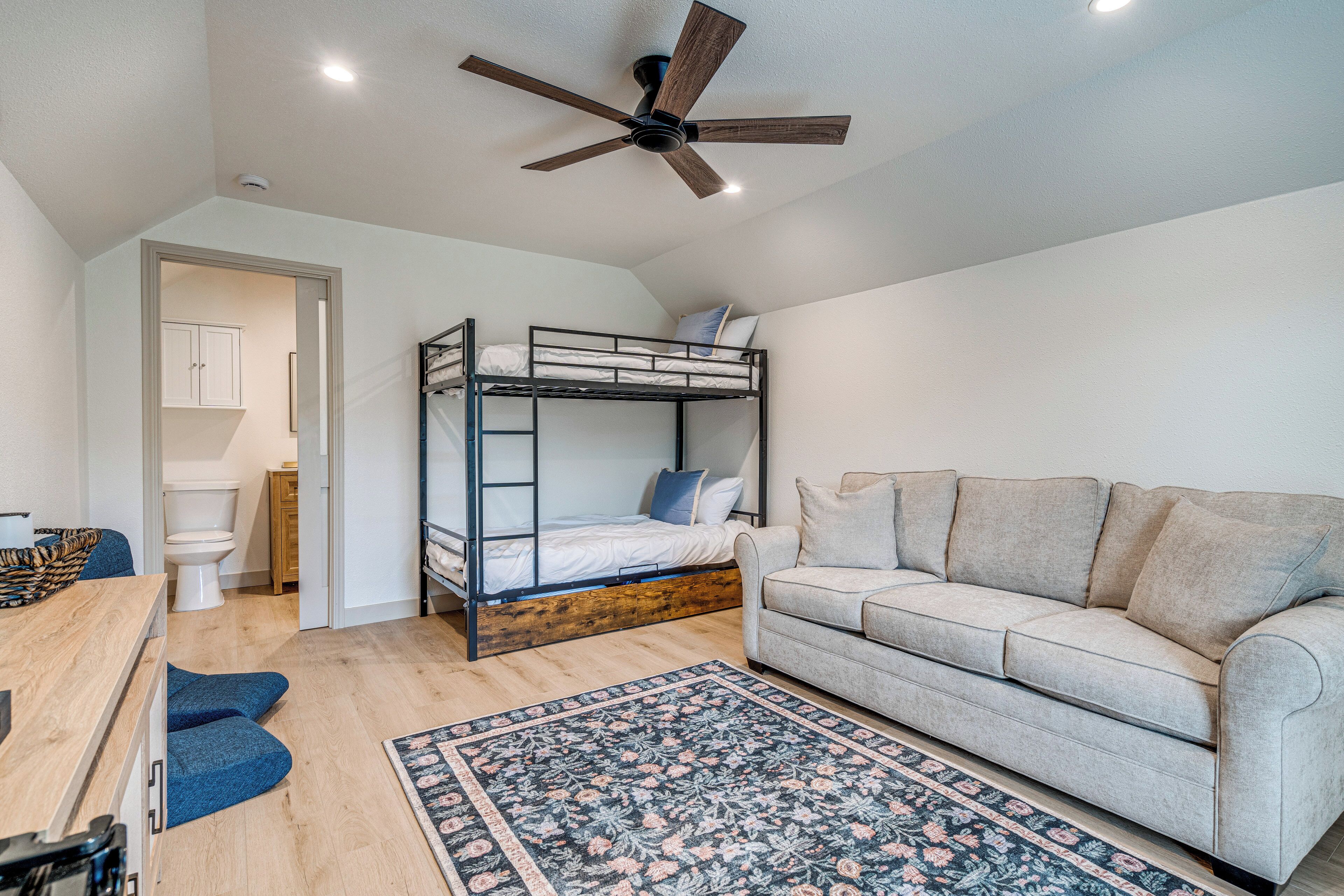 A bedroom with a bunk bed, a sofa, a wooden desk, and a patterned rug.