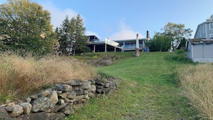 En stenvæg, græsplæne og moderne bygninger med store vinduer og skorstene.