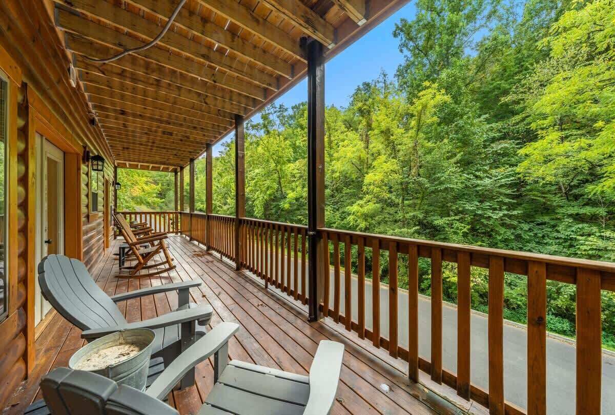 Una terraza de madera con sillas Adirondack y vista a un área boscosa.