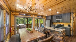 A wooden cabin interior with a dining area, kitchen, and large windows.