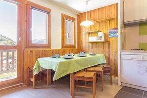 A dining area with a table set for four, wooden walls, a window, and a kitchen area with a refrigerator.