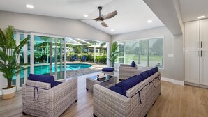 A modern living room with wicker furniture, a ceiling fan, and a view of a swimming pool.
