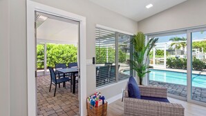 A modern living room with a view of a swimming pool, a wicker sofa, a dining table, and a basket of items.