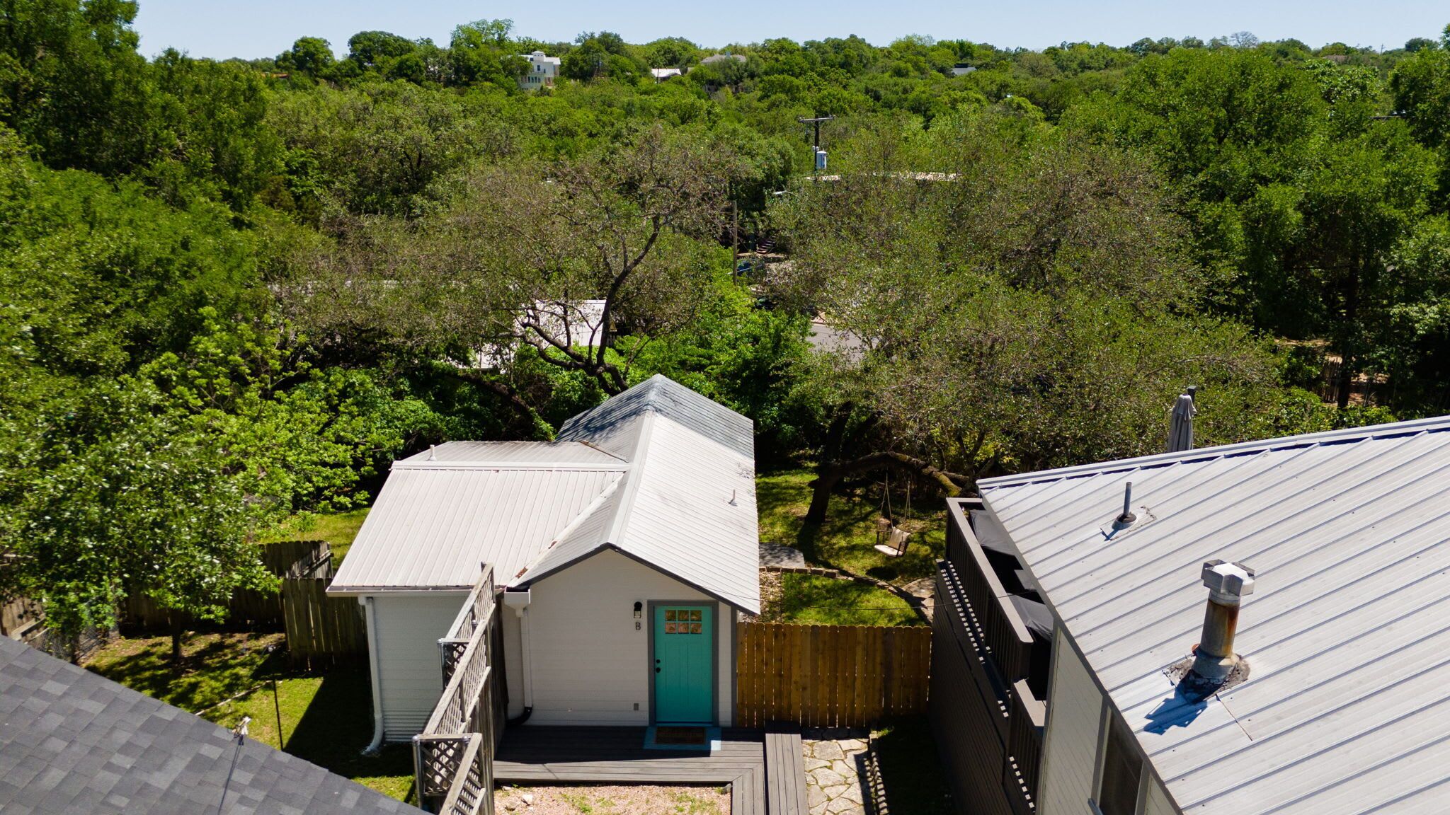 A residential area with a small house featuring a green door, surrounded by lush greenery and a wooden fence.