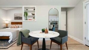 A modern bedroom with a bed, bedside table, lamp, and a small round table with chairs. - Chic Studio | Walkable to SoCo! (Austin)