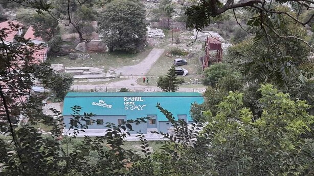 A building with a blue roof and a sign that reads "RAHUL HOME SOYAY" and a phone number. - Rahul Homestay (Sainj)