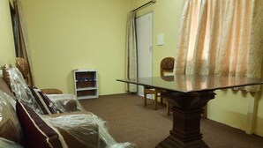 A room with a glass-top table, a wooden chair, and a sofa covered in plastic. - Rahul Homestay (Sainj)