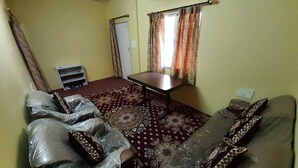 A room with a patterned carpet, a table, and two couches with pillows. - Rahul Homestay (Sainj)