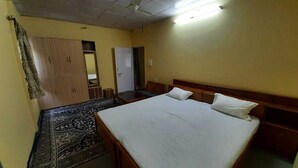 A hotel room with a large bed, a wardrobe, a desk, and a ceiling fan. - Rahul Homestay (Sainj)