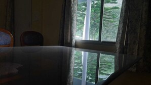 A room with a large window, a chair, and a table. - Rahul Homestay (Sainj)