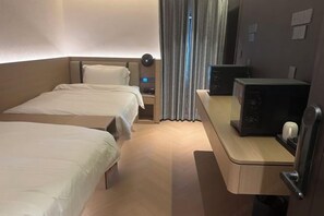 A hotel room with two beds, a desk with a computer, and a window with curtains.