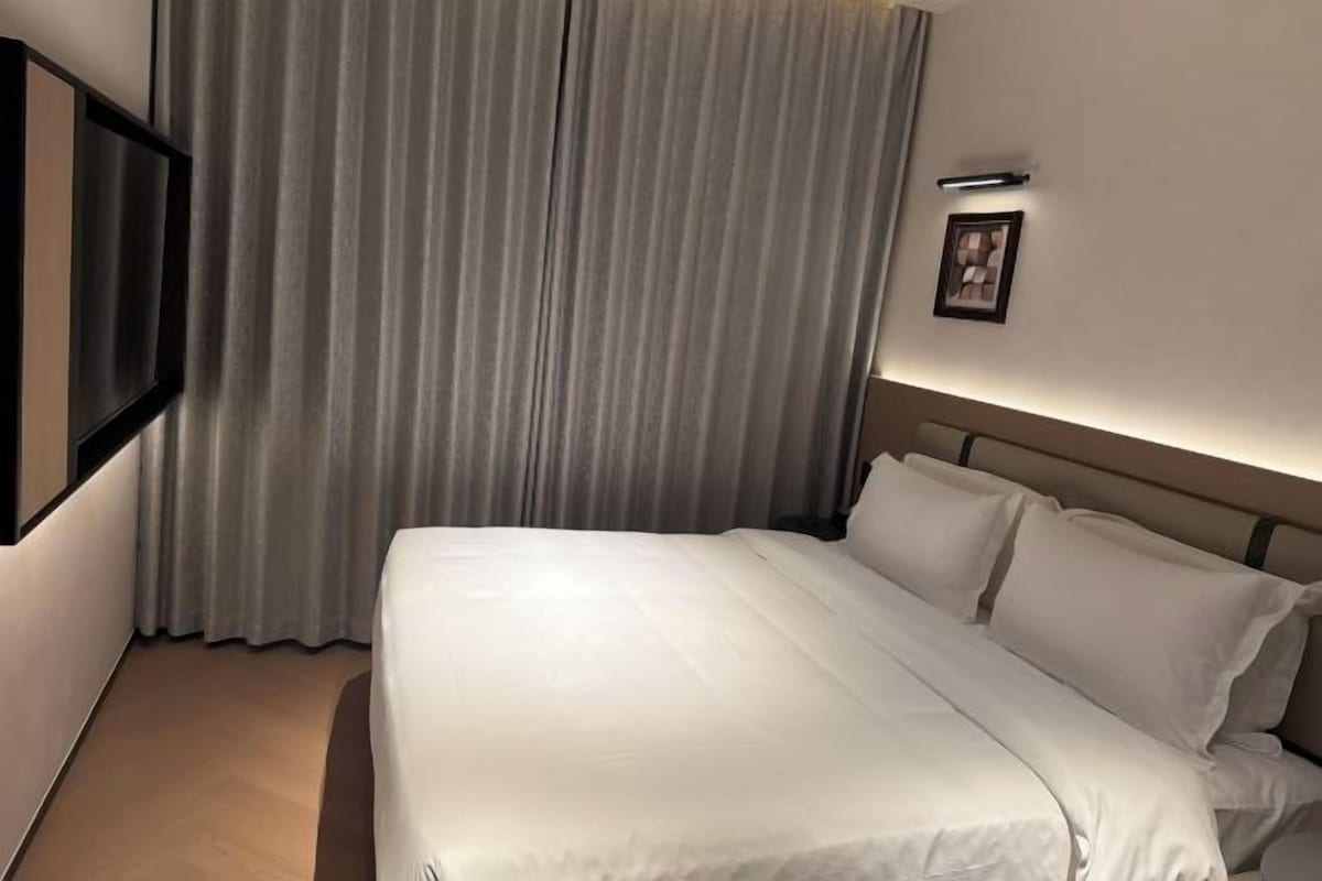 A hotel room with a bed, curtains, a wall-mounted picture, and a light fixture.