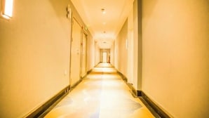 A long, narrow hotel corridor with doors on both sides, recessed lighting, and a carpeted floor.