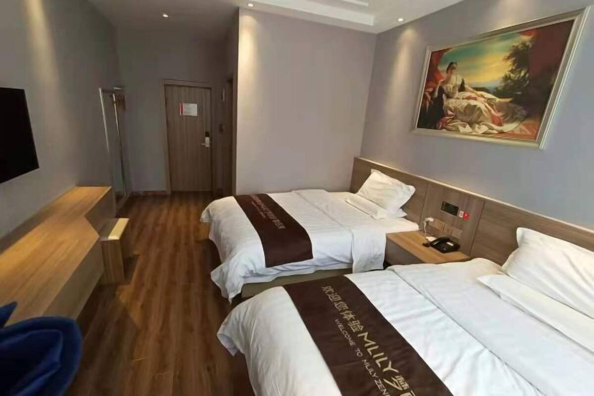 A hotel room with two beds, a wooden floor, a painting on the wall, and a flat-screen TV.