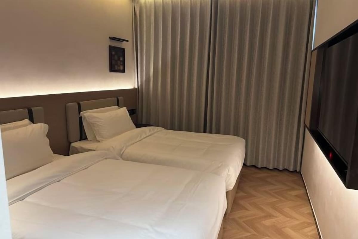 A hotel room with two beds, a TV, and a window with curtains.