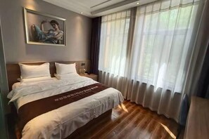 A hotel room with a large bed, a nightstand, a painting on the wall, and sheer curtains on the window.