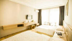 A hotel room with two beds, a wooden bedside table, a mounted TV, and a window with curtains.