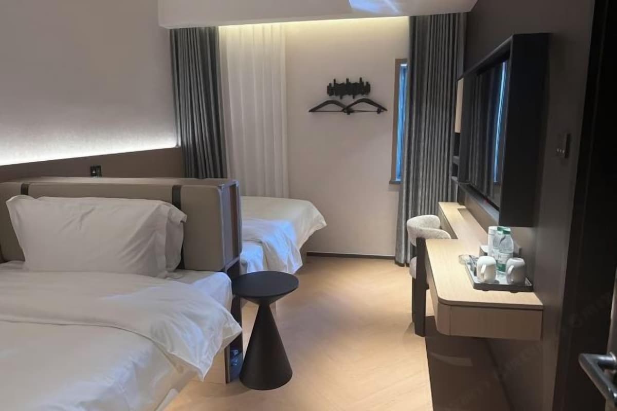 A hotel room with two beds, a desk with a chair, a flat-screen TV, and a mirror.
