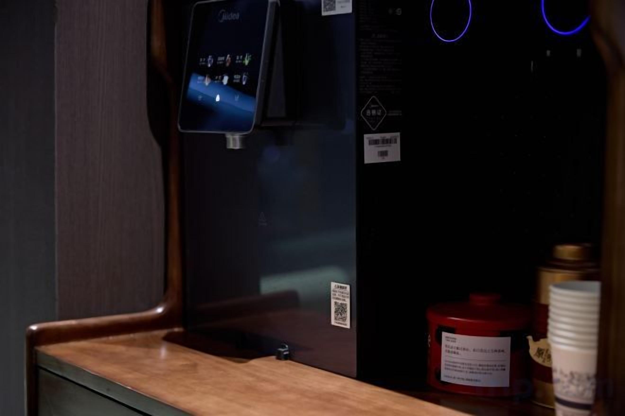 Een waterdispenser met een digitaal display, een rode container en een beker op een aanrecht.
