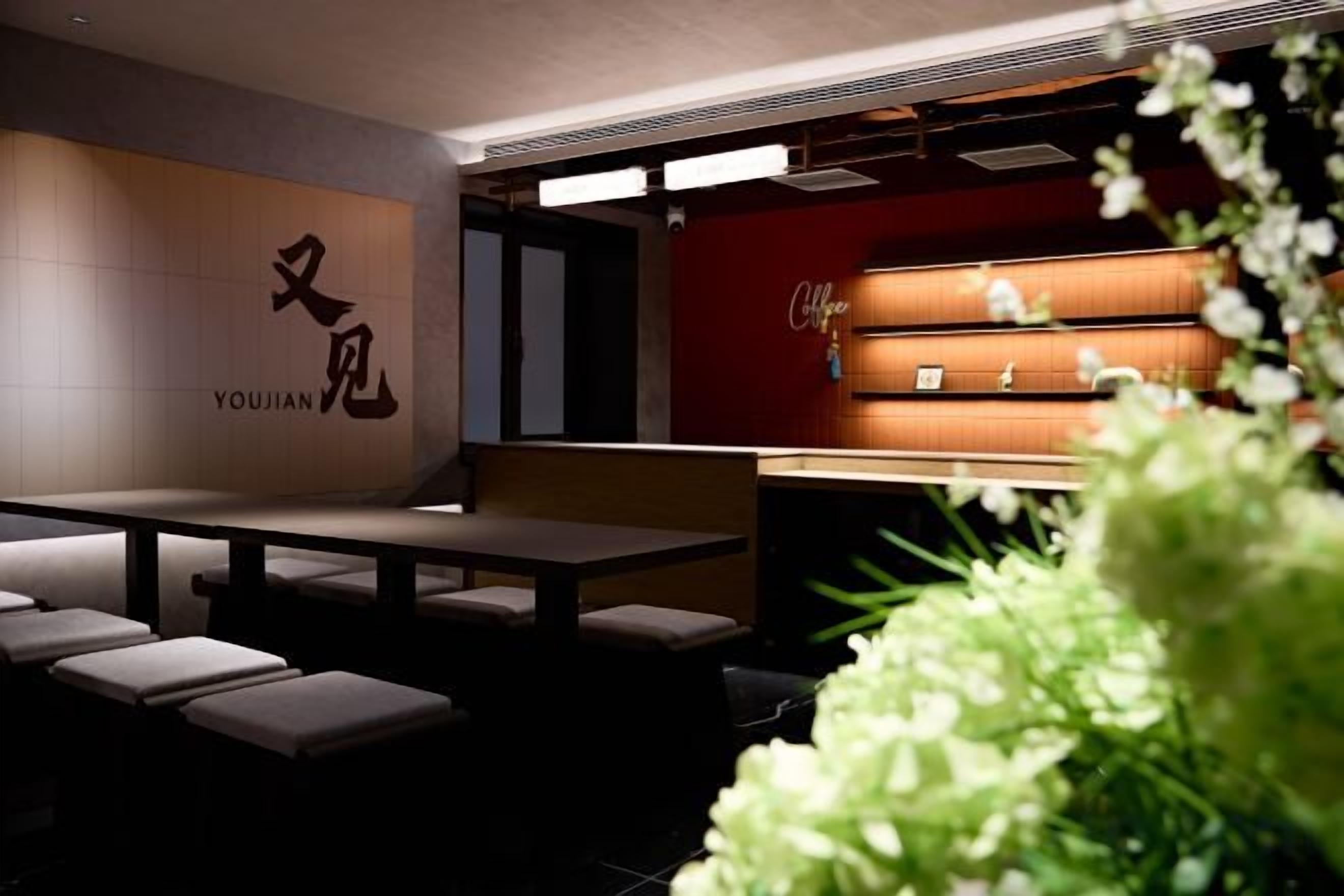 Een restaurant interieur met een minimalistisch ontwerp, met een lange toonbank, een zithoek en een muur met de naam 'YOUJIAN'.
