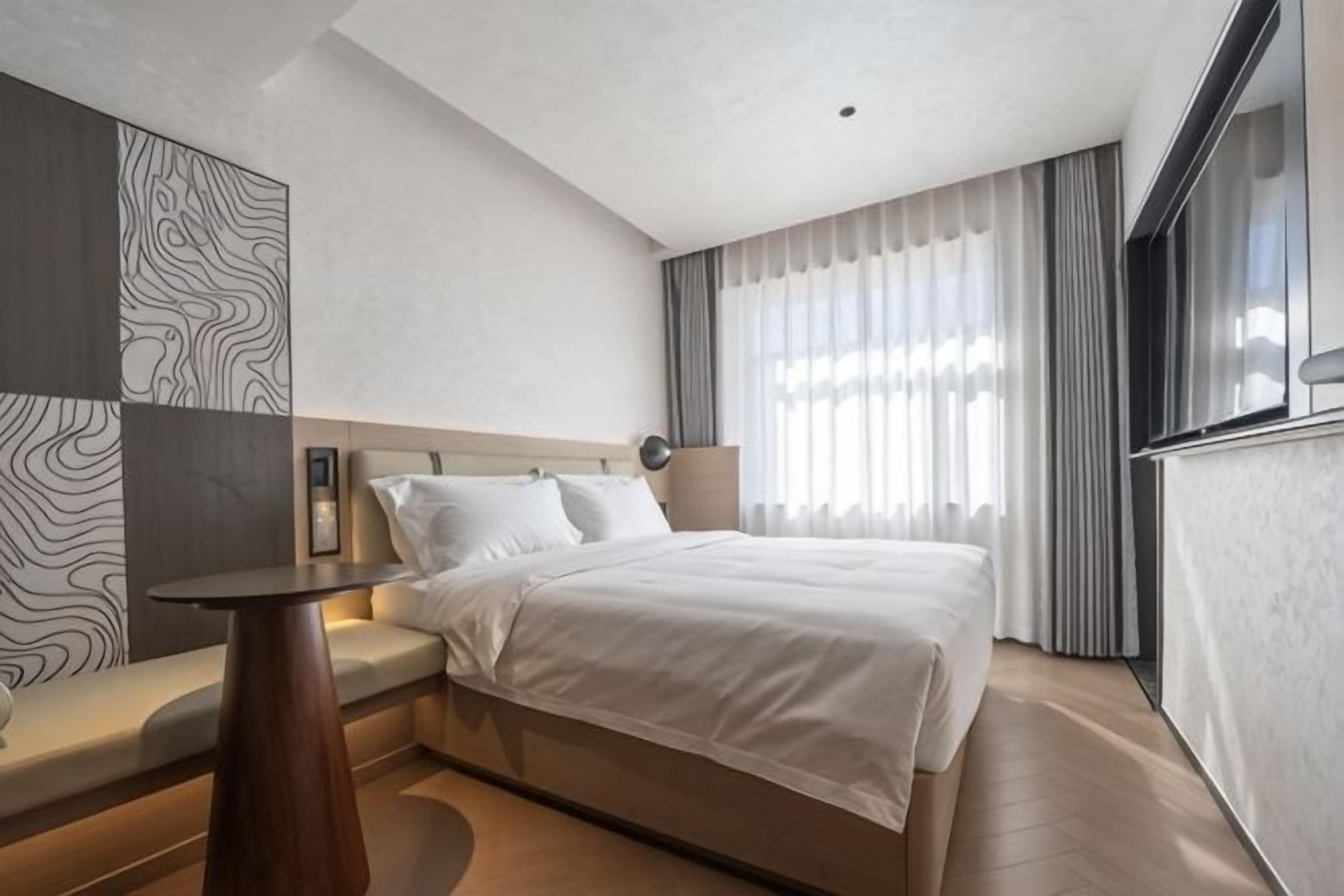 Habitación de hotel moderna con una cama grande, una mesita de noche, un área de estar y vistas al exterior.