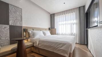Habitación de hotel moderna con una cama grande, una mesita de noche, un área de estar y vistas al exterior.