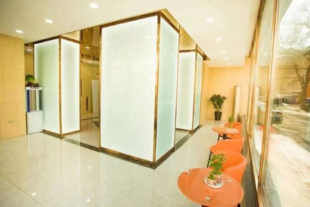 A modern hotel lobby with a glass partition, orange seating area, and a view of the outdoors.
