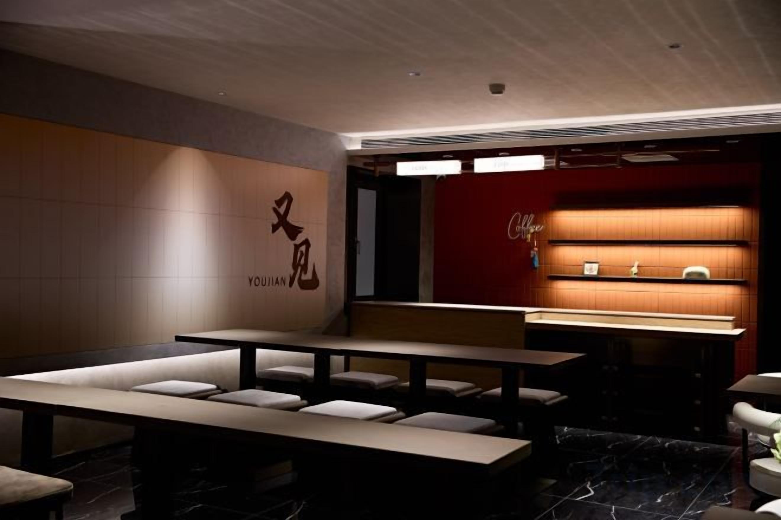 A restaurant with a modern interior, featuring a counter with a red backdrop and a seating area with tables and benches.