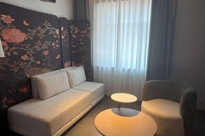 A hotel room with a sofa, a round table, and a chair.