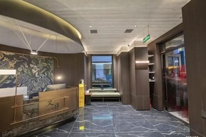A hotel lobby with a reception desk, seating area, and a view of the street.