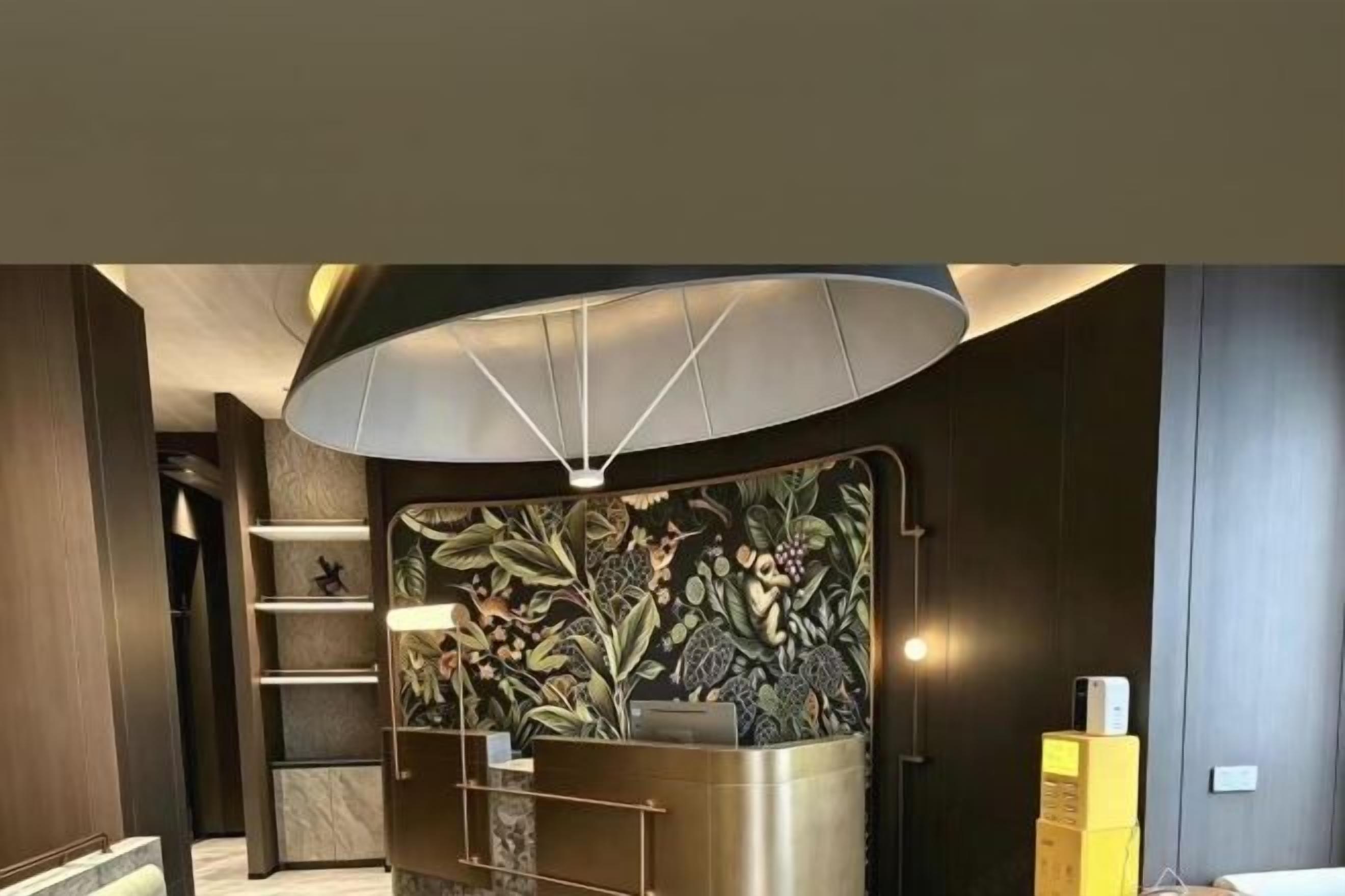 A reception area with a modern design, including a reception desk, a wall with a floral pattern, and a large overhead light fixture.