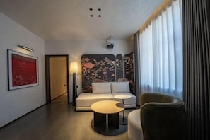 Een moderne hotelkamer met een bank, twee bijzettafels, een lamp en een groot raam met gordijnen.