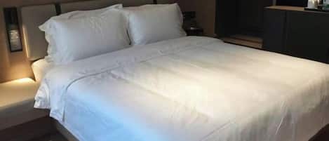 Una cama bien hecha con ropa de cama blanca, una mesita de noche con lámpara y un aparador de color oscuro.