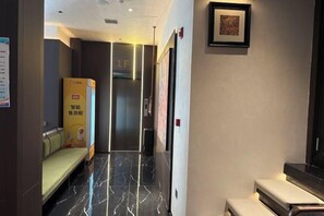 A hotel hallway with a reception desk, a bench, a vending machine, and a framed picture on the wall.