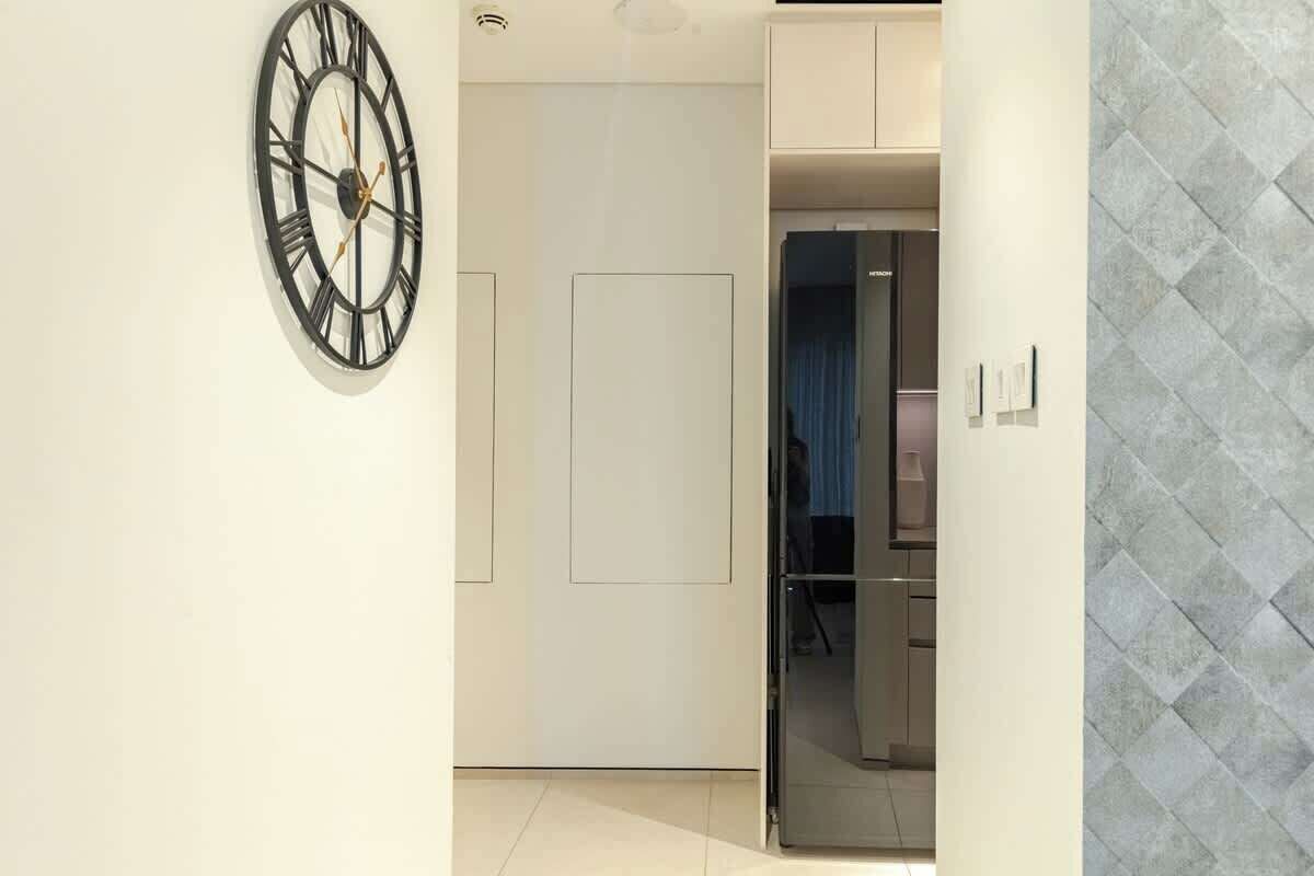 A hallway with a modern clock, a door, and a glass partition leading to a room.