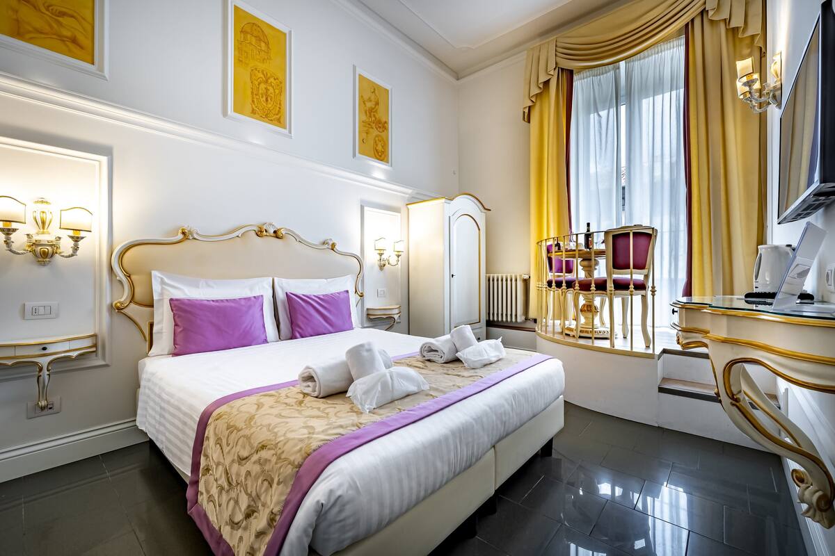 A luxurious hotel room with a large bed, a vanity with a mirror, and a television.